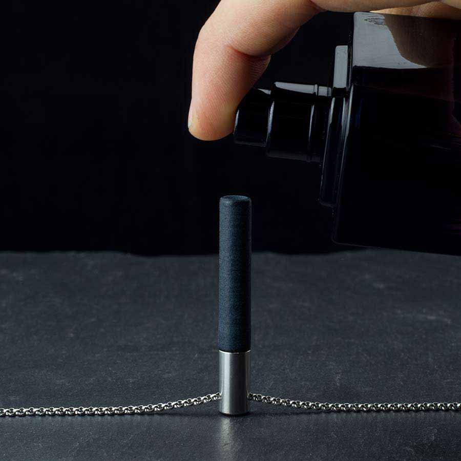 Spraying black and silver Lockstone pendant on slate surface with fragrance